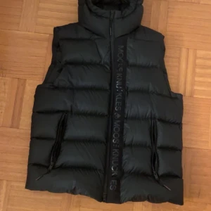 Svart dunväst från Moose Knuckles - Svart dunväst från Moose Knuckles med hög krage och breda. Nypris 6000kr har använts under en höst och är i nyskick.