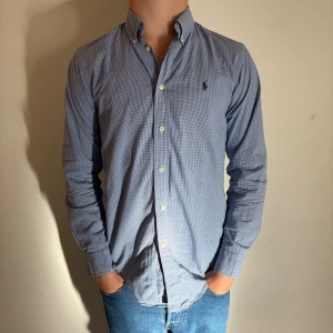 Blårutig skjorta från Ralph Lauren - Snygg blårutig skjorta från Ralph Lauren med klassisk button-down krage och broderad logga på bröstet. Skjortan har vita knappar och är tillverkad i mjuk bomull. Perfekt passform med långärmade ärmar och stilren look. Hör av dig vid frågor! Plagget skickas inom 24h efter köp. Modellen på bilden är 173 och väger 61 kg. Den sitter lite tajt! (Plagget passar som en herr XS)
