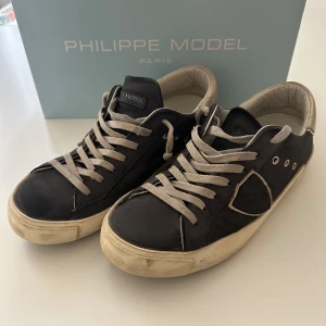 Philippe Model, Storlek 39 - Mörk blåa Philippe Model sneakers i mocka med beige detaljer och snörning. Klassisk låg modell med rund tå och platt. Priset är inte fast och kan diskuteras. Hör av er om några funderingar. Skicket är 7/10. Storlek 39 men passar 40