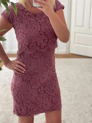 Lila spetsklänning från Saint Tropez - Supersöt kort klänning i lila från Saint Tropez. Klänningen har blommigt spetsmönster, rund halsringning och korta ärmar. Figurnära passform och helfodrad för en snygg siluett. Perfekt för dig som gillar romantiska detaljer och vill sticka ut.