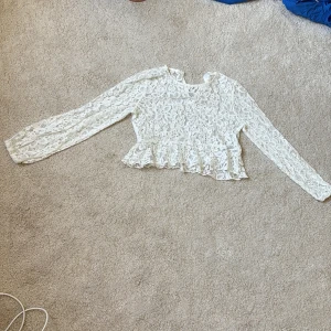 Vit spetsblus från H&M med volang - Supersöt vit blus från H&M i spets med blommigt mönster. Modellen är croppad med volang nertill och har långa ärmar. Har använts 3-4 gånger så är i nyskick!🩷