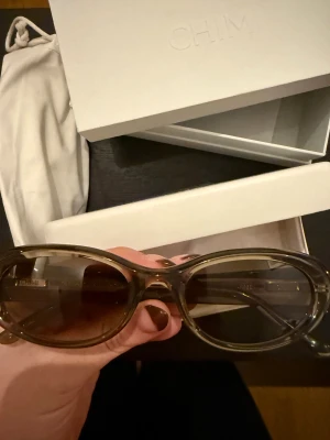 Ovala gröna solglasögon från CHIMI - Snygga solglasögon från CHIMI i transparent grön plast med ovala bågar och bruna tonade glas. Kommer med originalförpackning, hårt fodral och tygpåse. Perfekt accessoar för att lyfta din stil.