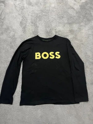 Svart långärmad tröja från BOSS - Svart långärmad tröja från BOSS med stor gul logotyp på bröstet. Skicka gärna bud