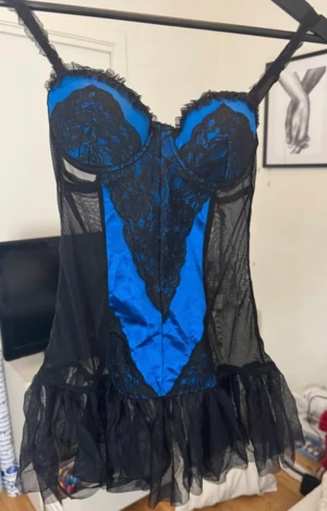 Blå och svart spetsklänning Native Intimates - Supersnygg kort klänning från Native Intimates i blått och svart med transparent mesh och spetsdetaljer. Klänningen har smala axelband, markerade kupor och volangkant nertill. Perfekt för dig som gillar en edgy och unik look.