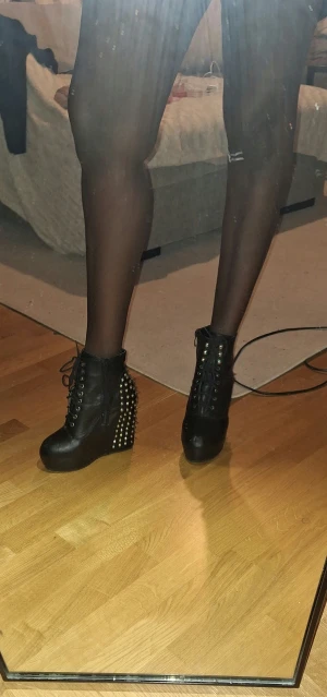 Jeffeey Campbell lilnande Svarta boots med nitar och platå - Säljer ett par svarta boots med höga kilklackar och rund tå. Skorna har snörning framtill, dragkedja på sidan och är täckta med silvriga nitar och spikes på hälen. Tillverkade i syntetmaterial med cool rockig vibe, perfekta för dig som gillar att sticka ut.