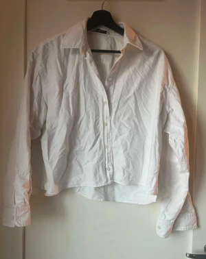 Vit klassisk skjorta med knappar - Vit skjorta med klassisk krage och knappar framtill. Skjortan har lång ärm med manschett och är tillverkad i ett lätt bomullstyg. Passformen är normal och modellen är enkel och tidlös, perfekt för dig som gillar stilrena plagg.