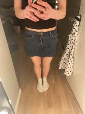 Mörkblå jeanskjol med volang - Säljer en mörkblå jeanskjol som jag själv har gjort med volang nedtill. Kjolen har klassiska jeansfickor fram och bak, bälteshällor och stängs med knapp och dragkedja. Perfekt för dig som gillar en casual och trendig stil. Kjolen är lite fel sydd på ena sidan och sitter lite konstigt på ena sidan pågrund av sy felet men inget man riktigt märker av!