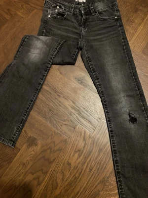 Svarta jeans med slitning - Snygga svarta jeans med tvättad look och slitning på ena benet. Klassisk femficksmodell med raka ben och normal passform. Perfekta för dig som gillar en lite tuffare stil.