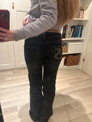 Svarta bootcut jeans med strassdetalj - Säljer ett par svarta bootcut jeans med låg midja och snygg strassdetalj på bakfickan. Använd kanske 3 gånger. Midjemåttet är 36-37 cm och innerbenslängden är ca 79 cm