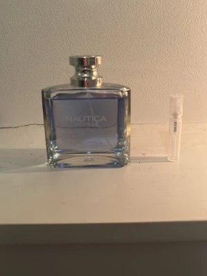 Nautica Voyage parfym blå glasflaska - Fräsch parfym från Nautica i modellen Voyage. Flaskan är rektangulär i genomskinligt glas med ljusblå vätska och har ett silverfärgat lock. Perfekt för dig som gillar marina och friska dofter.