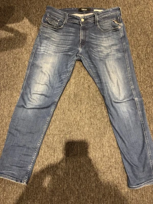 Blå Replay jeans med raka ben - Säljer ett par blå jeans från Replay med klassisk femficksmodell och raka ben. Jeansen har snygga slitningar och ljusare partier framtill och baktill för en cool, avslappnad look. Tillverkade i mjuk bomullsdenim med dragkedjegylf. W32 L30