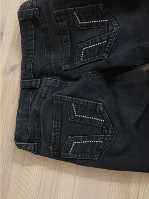 Svarta jeans med nitar från Gina Tricot - Svarta jeans från Gina Tricot med raka ben och snygga nitar på bakfickorna som ger extra edge. Klassisk femficksmodell i mjukt denimtyg. Perfekta för dig som vill ha en cool och stilren look.