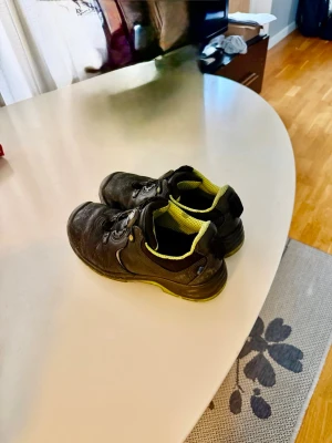 Svarta arbetsskor med grön sula - Ett par begagnade Arbesko skyddsskor. Skorna är i bra skick och redo för användning. 