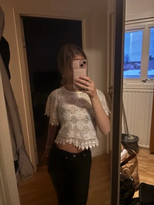 Vit spetsig croppad blus - Säljer en vit croppad blus med vacker spets och korta ärmar. Blusen har fina volangdetaljer vid ärmslut och nederkant, vilket ger en romantisk känsla. Perfekt att styla med höga jeans eller kjol.