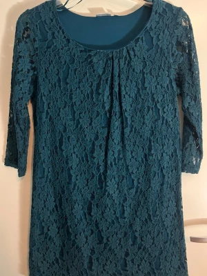Mörkblå spetsklänning med trekvartsärm - Snygg mörkblå klänning i spets med trekvartsärm och rund halsringning. Klänningen har ett vackert blommigt spetsmönster och är perfekt för dig som vill ha en elegant look. Fodrad underklänning och stretchigt material för skön passform.