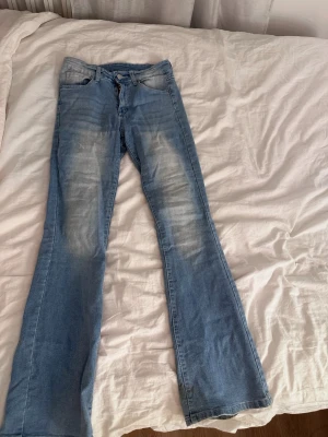 Ljusblå bootcut jeans med slitningar från Shein  - Säljer ett par ljusblå bootcut jeans med snygga slitningar framtill och bakfickor med dekorativa detaljer. Jeansen har klassisk femficksdesign och stängs med dragkedja och knapp. Perfekta för dig som gillar en avslappnad och trendig look. Från Shein