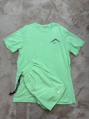 Nike Shortsset - Snyggt ljusgrönt set från Nike med t-shirt och shorts. T-shirten har rund hals och tryckt logga på bröstet, medan shortsen har resårmidja med svart dragsko och vit Nike-logga. Perfekt för en sportig och avslappnad stil. T-Shirt storlek: M Shorts storlek: S