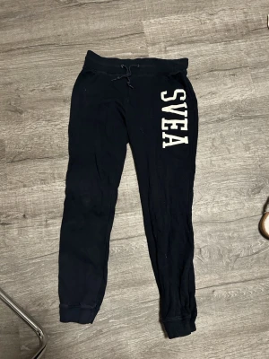 Svarta mjukisbyxor från SVEA - Mörkblå mjukisbyxor från SVEA med vitt tryck längs ena benet. Byxorna har resår och snörning i midjan samt muddar vid bensluten. 