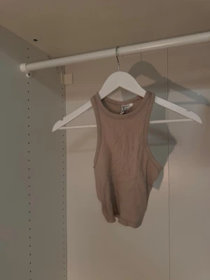 Beige ribbad linnetopp från Divided - Säljer en beige ribbad linnetopp från Divided. Toppen är ärmlös med rund halsringning och croppad passform. Perfekt att matcha med höga jeans eller kjol för en trendig look🤍.