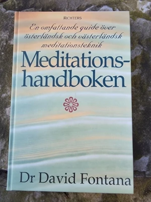 Meditationshandboken av Fontana - En omfattande guide över österländsk och västerländsk meditationsteknik av Dr David Fontana. Boken har ett mjukt pastellfärgat omslag med stora tydliga bokstäver och innehåller både teori och praktiska övningar för meditation, avslappning och personlig utveckling.