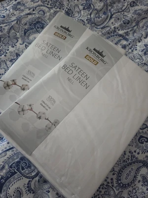 Vita sängkläder Kronborg Gold - Två paket vita sängkläder från Kronborg Gold, modell Sateen Bed Linen Nell. Tillverkade i 100% bomullssatin för en mjuk och lyxig känsla. Storlek 150x210 cm. Perfekt för dig som vill ha ett fräscht och stilrent sovrum.