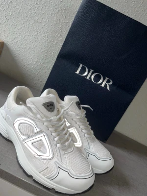 Vita Dior sneakers med mesh och skinn - Snygga vita sneakers från Dior med coola detaljer i mesh och skinn. Skorna har en chunky sula, stora CD-loggor på sidorna och klassisk snörning. Perfekta för dig som vill sticka ut med exklusiva och trendiga sneakers.