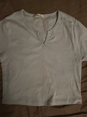 Ljusblå croppad topp från FB Sister - Säljer en ljusblå croppad topp från FB Sister. Toppen har korta ärmar och en unik v-ringad hals med liten slits framtill. Tillverkad i mjuk bomull som känns skön mot huden. Perfekt till jeans eller kjol för en enkel och snygg look.