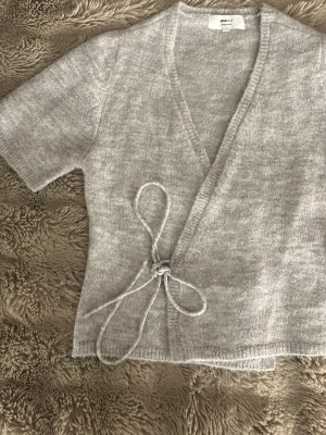 Grå omlottkofta  - Säljer en ljusgrå omlottkofta från Gina tricot med korta ärmar och knytband i sidan. Endast använd en gång. 