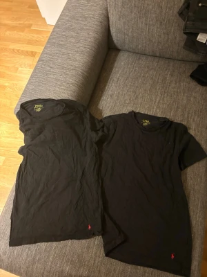 Svart t-shirt från Polo Ralph Lauren - Två svarta undershirts från Polo Ralph Lauren med klassisk passform och rund hals. Diskret röd logga broderad längst ner på framsidan. Perfekta basplagg för en clean och enkel stil. St M passar S