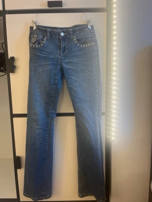 Blå jeans med nitar och broderi - Snygga blå jeans med raka ben och coola detaljer som nitar och broderi på fickorna. Jeansen har normal passform och är perfekta för dig som vill sticka ut lite extra. Klassisk femficksmodell i jeansmaterial.