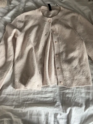Ljusbeige kofta från H&M - Mysig ljusbeige kofta från H&M i mjukt material. Rund halsringning, ribbade muddar och knappstängning framtill. Perfekt att slänga över en topp för en enkel och clean look.