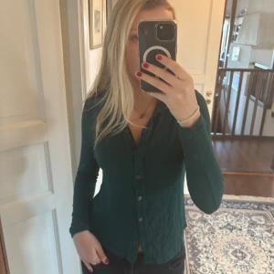 Mörkgrön ribbad skjorta  - Säljer en mörkgrön, figurnära skjorta med långa ärmar och knäppning framtill.