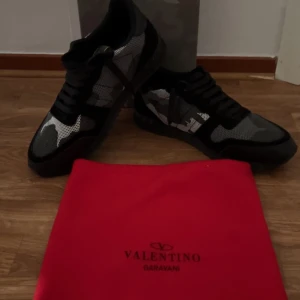 Valentino Garavani Rockrunner sneakers - Snygga Valentino Garavani Rockrunner sneakers i svart och grått med camouflage-mönster. Skorna har svarta snören, platt sula och detaljer i mocka och skinn. Perfekt för dig som gillar exklusiva och trendiga sneakers med unik design.