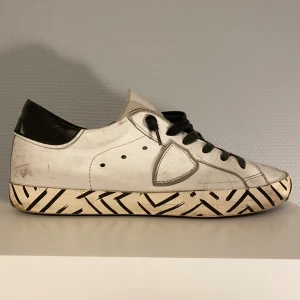 Philippe Model skor - Säljer dessa vita Philippe Model skorna med svarta detaljer på sulan. Skorna kommer i stl 40 och är i hyfsat bra skick, de mesta slitningarna är design. Undersulan är dock lagad med lim eftersom den brast lite vid hälen. Hör av er vid frågor!