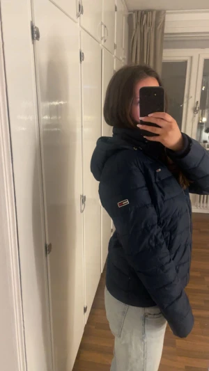 Mörkblå pufferjacka Tommy Hilfiger - Snygg mörkblå pufferjacka från Tommy Hilfiger med huva och dragkedja framtill. Jackan har även en päls till luvan som kommer med