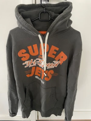 Mörkgrå Superdry hoodie - Säljer en mörkgrå hoodie från Superdry i storlek M, modellen är ca 180cm. Hör av dig vid funderingar 