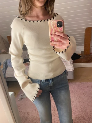 Vit långärmad tröja med svarta detaljer - Säljer en vit långärmad tröja med svarta sömdetaljer längs halsringning och ärmslut. Tröjan har en snygg, lite utsvängd ärm och sitter figurnära. Materialet känns mjukt och stretchigt, perfekt för dig som gillar stilrena plagg med en twist.