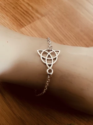 By prisförslag - Silvrigt armband med keltisk knut - Stilrent armband i silverfärgad metall med en keltisk knut som detalj i mitten. Kedjan är tunn och smidig, och knuten har en snygg geometrisk design som ger en unik vibe. Perfekt för dig som gillar minimalistiska och coola accessoarer.