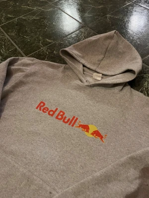Grå Red Bull hoodie  - Säljer denna gråa hoodie med ett Red Bull tryck. Storlek S/XS. Inga hål eller defekter, mycket bra skick. Hör av dig vid flera frågor eller flera bilder