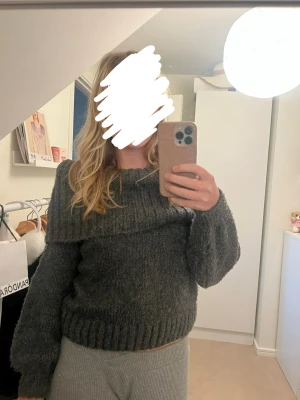 Mörkgrå offshoulder stickad tröja - Säljer en mysig mörkgrå stickad tröja med offshoulder-design och bred ribbad kant upptill. Perfekt för kalla dagar när du vill ha på dig något bekvämt. 