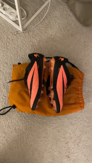 Nike Hypervenom Phantom fotbollsskor - Säljer ett par Nike Hypervenom Phantom fotbollsskor i svart och orange med coola döskalle-detaljer på hälen. Skorna har snörning och platt sula med dobbar för gräsplan. Ovandelen är tillverkad i syntetmaterial med textur för bättre bollkontroll.
