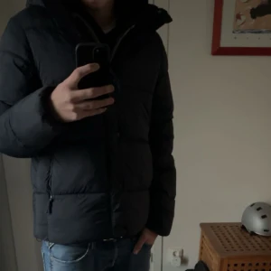 Mörkblå pufferjacka med huva - Säljer en mörkblå pufferjacka med huva och dragkedja. Jackan är vadderad och har en klassisk, Snygg och enkel design som funkar till det mesta. Väldigt varm perfekt för denna vinter 