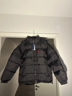 Svart pufferjacka från Polo Ralph Lauren - Polo Ralph Lauren vinterjacka – Ny!  Säljer en helt ny Polo Ralph Lauren vinterjacka, endast provad. Fick den i present men tyvärr är den för kort i armarna för mig.  Storlek M, men skulle säga att den sitter lite mer som en S.  Jackan är varm, skön och av hög kvalitet, precis som man förväntar sig av Ralph Lauren.  Kan skickas, och pris kan diskuteras vid snabb affär.  Hör av dig vid intresse!