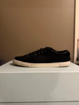 Svarta sneakers från Lanvin Paris - Lanvin  sneakers i svart mocka med blanck  tå och vit platt sula. Klassisk rund tå och snörning med metallöglor. Snygg kontrast mellan matt mocka och glansig lackdetalj framtill. Perfekt för dig som gillar stilrena och lyxiga sneakers.
