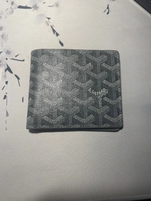 Svart Goyard plånbok med mönster - Snygg svart plånbok från Goyard med deras ikoniska grafiska mönster i vitt. Plånboken är stilren och har en klassisk fyrkantig form, perfekt för kort och sedlar. Materialet är skinn och designen är riktigt clean och modern.
