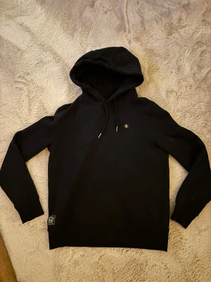 Svart hoodie från Morris! Använd nån enstaka gång, inga defekter.Ordinarie pris 1600kr, mitt 750. Storleken är xs men sitter som en s. - Svart hoodie från Morris med huva och snörning. Liten broderad logga på bröstet och patch vid nederkanten. Mjuk bomullskvalitet och långa ärmar. Perfekt för chill dagar eller när du vill ha en clean look.
