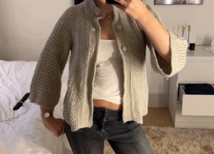 Beige stickad kofta med knappar - Säljer en beige stickad kofta med struktur och stora dekorativa knappar framtill. Koftan är trekvartsärmar och en rund halsringning. Perfekt att slänga över en fin topp för en snygg look.