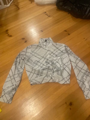 Vit rutig skjorta från FB Sister XS - Snygg vit skjorta från FB Sister i storlek XS med svart rutigt mönster och textdetaljer. Skjortan har klassisk krage, långa ärmar och knappar framtill. Perfekt för dig som gillar en trendig och modern stil.