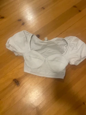 Vit croppad topp från Monki - Säljer en vit croppad topp från Monki i storlek S. Toppen har puffiga korta ärmar och markerade kupor framtill för en snygg siluett. Materialet är mjukt och stretchigt, perfekt för att skapa en trendig look. Passar dig som gillar stilrena och feminina detaljer.