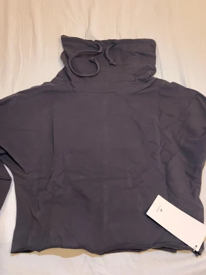 Mörkgrå hoodie från A Line - Säljer en stilren mörkgrå hoodie från A Line med huva och snörning. Tröjan har långärmade ärmar och är gjord i mjuk bomull. Perfekt för chill dagar och enkel att matcha med jeans eller joggers. Taggen sitter kvar.